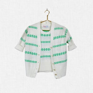 May include: A white short-sleeved cardigan and matching sleeveless top set featuring a repeating green geometric pattern of horizontal stripes, chevrons, and diamond shapes. The cardigan has a button-front closure and ribbed trim.