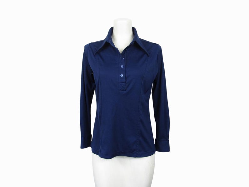 May include: A navy blue long-sleeve shirt with a collared neckline and three buttons. The shirt is displayed on a white mannequin. The shirt has a tailored fit and is made of a smooth fabric. The shirt is a classic style.