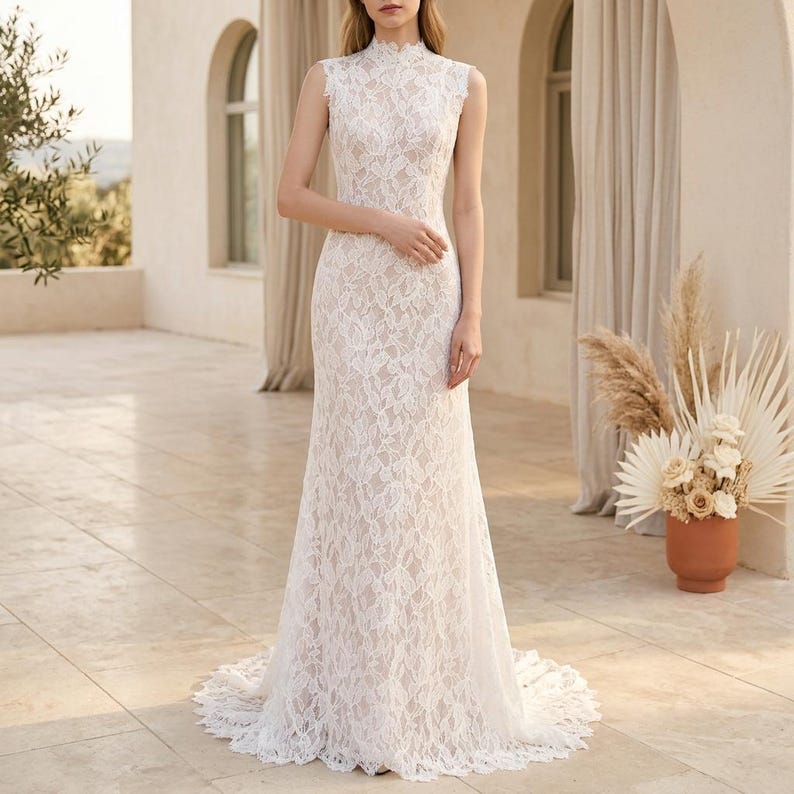 May include: An ivory lace wedding dress with a high neckline and sleeveless design. The floor-length gown has a fitted shape that gently widens towards the hem, forming a small train. The dress is entirely covered in detailed lace, giving it a delicate and romantic appearance.