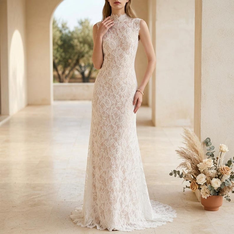 May include: An ivory lace wedding dress with a high neckline and sleeveless design. The dress has a fitted shape and a subtle train. The intricate floral lace is visible. The bride is standing in an arched hallway. A floral arrangement is in a terracotta pot.