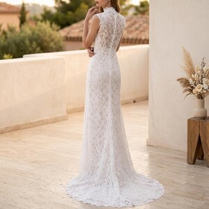 May include: A white lace wedding dress with a high neckline and a long train. The sleeveless gown features intricate floral lace detailing and a fitted silhouette that flares out at the hem. Suitable for a wedding or special occasion.