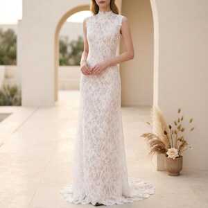 May include: A white lace wedding dress with a high neckline and sleeveless design. The dress is floor-length with a fitted bodice and a flowing skirt, complete with a subtle train. The entire dress is covered in an intricate lace pattern.