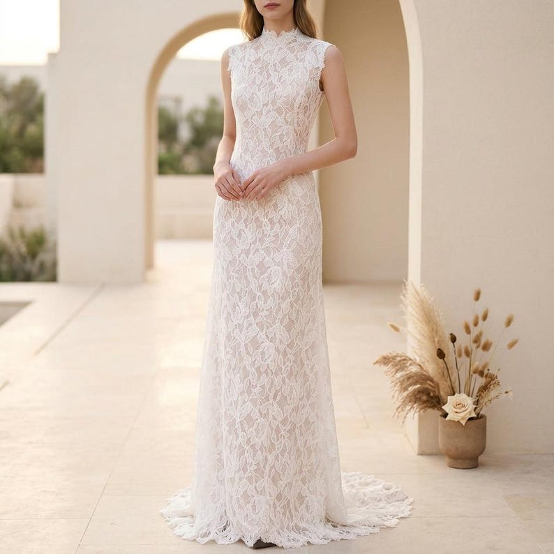 May include: A white lace wedding dress with a high neckline and sleeveless design. The dress is floor-length with a fitted bodice and a flowing skirt, complete with a subtle train. The entire dress is covered in an intricate lace pattern.