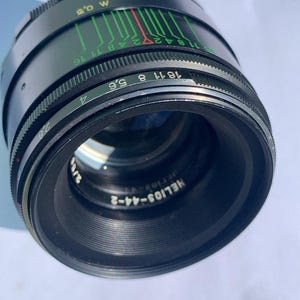 Puede incluir: Un objetivo Helios-44-2 58mm f/2 negro con una escala de apertura verde y roja. El objetivo está hecho en la URSS.