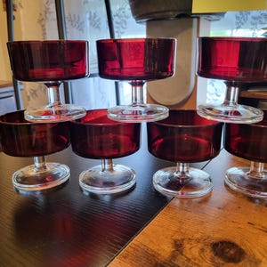 May include: Set of six clear glass dessert dishes with a red base. The dishes are stacked in a pyramid shape on a wooden table.