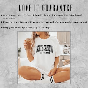 May include: White t-shirt with "NORTH CAROLINA TAR HEEL STATE" text in black. The person is holding a glass of iced coffee. The text "LOVE IT GUARANTEE" is at the top of the image.
