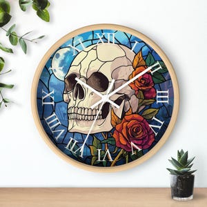 May include: A round wall clock with a wooden frame and a stained glass design. The clock face features a skull with roses and a moon in the background. Roman numerals mark the hours.