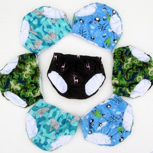 May include: Set of seven colorful and patterned cloth diapers. The diapers feature various designs, including penguins, fish, and abstract patterns.