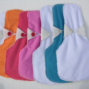 May include: Five reusable cloth pads in various colors, including orange, pink, light pink, teal, and white. The pads have a white fabric insert with a snap closure.