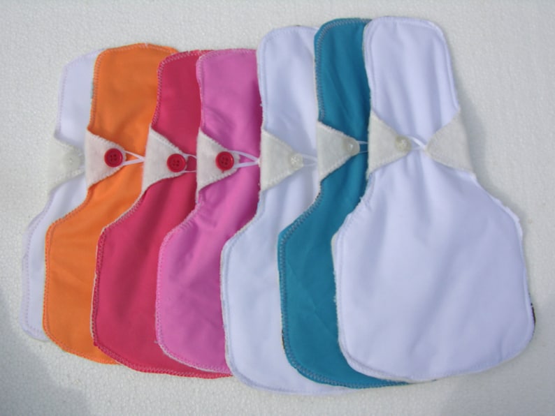 May include: Five reusable cloth pads in various colors, including orange, pink, light pink, teal, and white. The pads have a white fabric insert with a snap closure.