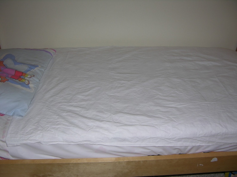 May include: A white bed sheet is neatly tucked into a wooden bed frame. A blue pillow with a colorful cartoon character is on the bed.