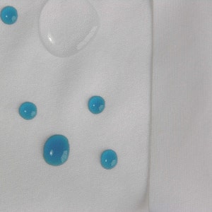 May include: A white fabric surface with five blue water droplets and a clear water droplet.