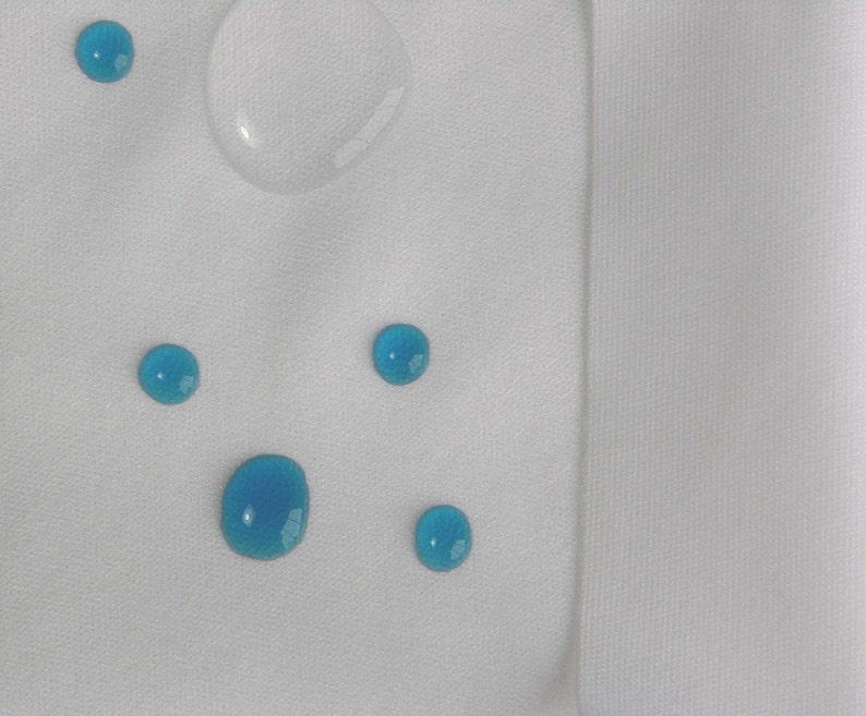 May include: A white fabric surface with five blue water droplets and a clear water droplet.