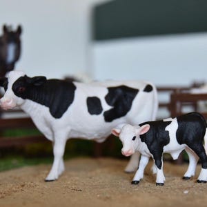 May include: A black and white cow figurine with a smaller black and white calf figurine. Both figurines are made of plastic and have realistic details.