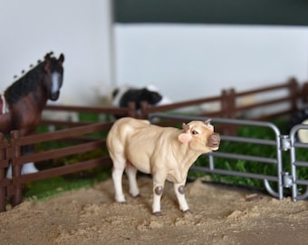 May include: A brown and white horse figurine standing behind a brown wooden fence. A light brown cow figurine with a white face is standing in front of the fence. The cow is looking to the right.