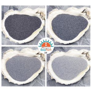 May include: Four oyster shells each containing a different shade of fine grey sand, ranging from dark charcoal to light silver. A circular logo in the centre features a lighthouse graphic with the text Mariana's SeaFort 34 in blue and orange.