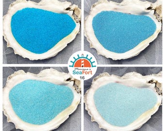 May include: Four oyster shells filled with blue sand in varying shades. The shells are arranged in a square, with the text "Mariana's SeaFort 16" in the center. The sand colours range from light to dark blue.
