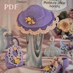 Può includere: Un cappello di uncinetto viola con un bordo di pizzo, una borsa di uncinetto viola con un bordo di pizzo e un fiore giallo, e una scarpa di uncinetto viola con un bordo di pizzo e un fiore giallo. Gli articoli fanno parte della "Stepping Through Time Collection" e di "Annie's Miniature Shoe Society".
