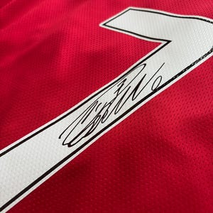 Puede incluir: Camiseta de f&uacute;tbol roja con detalles blancos, que muestra el n&uacute;mero 7 en blanco con un contorno negro. La camiseta tiene una firma sobre el n&uacute;mero. La palabra "RONA" es visible en la parte superior.