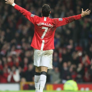 Puede incluir: Un futbolista con una camiseta roja con el nombre "Ronaldo" y el n&uacute;mero "7" en la espalda, con los brazos extendidos en celebraci&oacute;n. Viste pantalones cortos blancos, calcetines blancos y negros y botas naranjas. El fondo muestra una multitud borrosa.