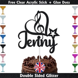 May include: A black glitter cake topper with the name "Jenny" in cursive, featuring a heart and treble clef design, and a star. The topper is on a chocolate cake. The image includes text: "Free Clear Acrylic Stick + Glue Dots" and "Double Sided Glitter."