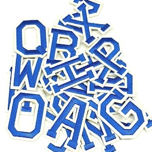 May include: A pile of blue and white embroidered letter patches. The letters are in a varsity style with a white border and a blue interior. The letters are scattered on a white background.
