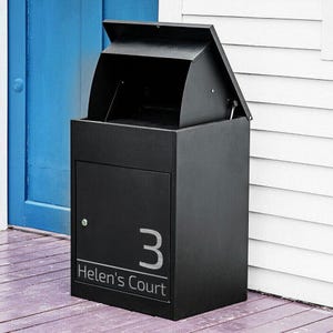 May include: A black, contemporary mailbox with an open top and a hinged lid. The front door displays the number "3" and the text "Helen's Court" in silver. The mailbox is on a wooden porch next to a blue door.