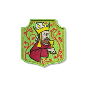 Puede incluir: Un parche bordado en forma de escudo que muestra una figura con barba marrón, una corona amarilla y una túnica roja. La figura sostiene un cáliz amarillo sobre un fondo verde claro decorado con patrones de enredaderas rojas y un borde verde.