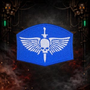 Könnte beinhalten: Blauer Aufnäher mit einem weißen Emblem, das einen geflügelten Schädel, ein Schwert und ein Kreuz zeigt. Der Aufnäher hat eine schildförmige Form mit weißen Stickdetails. Das Design ist ein stilisiertes Emblem.