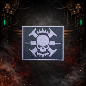 May include: A rectangular patch with a white skull and crossed tools design on a dark gray background. The skull has a crown and is surrounded by stylized tools. The patch is likely for clothing or accessories.