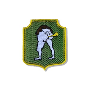 May include: An embroidered shield-shaped patch with a green background and a yellow border. The design features a pale blue figure with brown hair, standing on two legs, bending over to hold a yellow trumpet to its rear end.