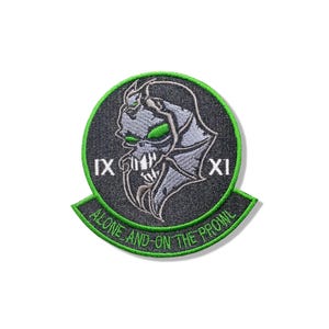 May include: A circular embroidered patch with a black background and a bright green border. It features a grey skull-like creature with green eyes, the Roman numerals IX and XI, and the text ALONE AND ON THE PROWL in green lettering.