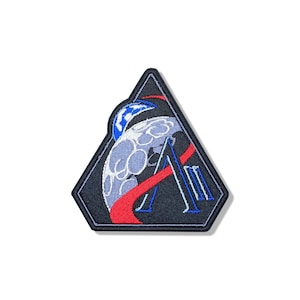 Peut inclure: Un écusson brodé triangulaire sur fond noir représentant une lune grise stylisée, un croissant bleu, un chemin rouge incurvé et une grande lettre A bleue accompagnée de deux lignes verticales bleues, le tout bordé d'un épais contour noir.