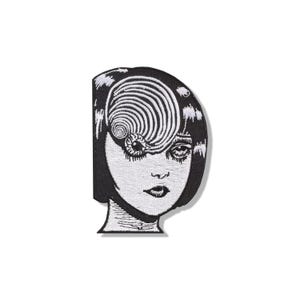 Pode incluir: Um emblema bordado a preto e branco com o retrato estilizado de uma pessoa com um corte de cabelo bob. O design inclui um padrão de espiral grande e proeminente que cobre um olho e a testa, com um único olho visível sob o redemoinho.
