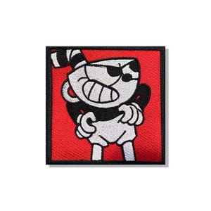 May include: A square embroidered patch featuring a cartoon character with a cup-shaped head, wide grin, and black and white color scheme. The character is set against a vibrant red background with a thick black border framing the entire design.