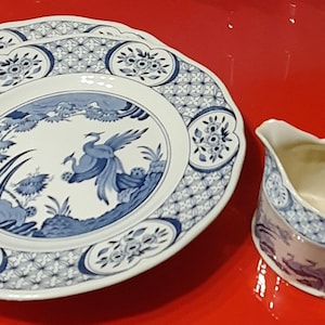 Puede incluir: Un juego de vajilla de porcelana azul y blanca con un delicado patrón floral y un diseño de pájaro. El juego incluye un plato grande, un plato pequeño y una jarra de crema.