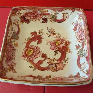 Puede incluir: Un plato de servir cuadrado de cerámica con fondo blanco y un diseño floral en tonos rosa, rojo y dorado.