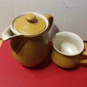 May include: A brown ceramic teapot with a lid and a matching brown ceramic mug. The teapot has a rounded body and a spout. The mug has a handle and a rounded body.
