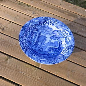 May include: A blue and white ceramic bowl with a floral pattern and a scenic design. The bowl is on a wooden surface.