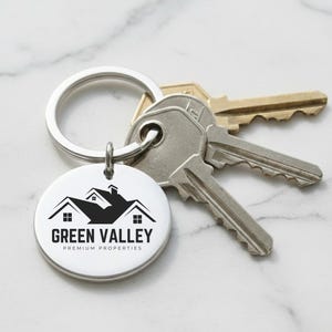 May include: A silver keychain with a round tag featuring the "Green Valley Premium Properties" logo in black. The keychain holds a set of keys. The background is a white marble surface.