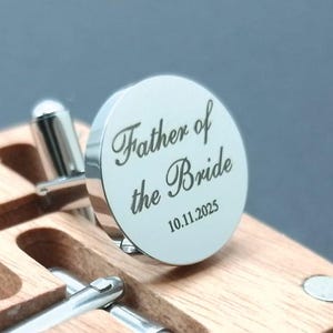 Round silver cufflinks engraved with the words “Father of the Bride” and the date “10.11.2025,” displayed on a wooden presentation box.