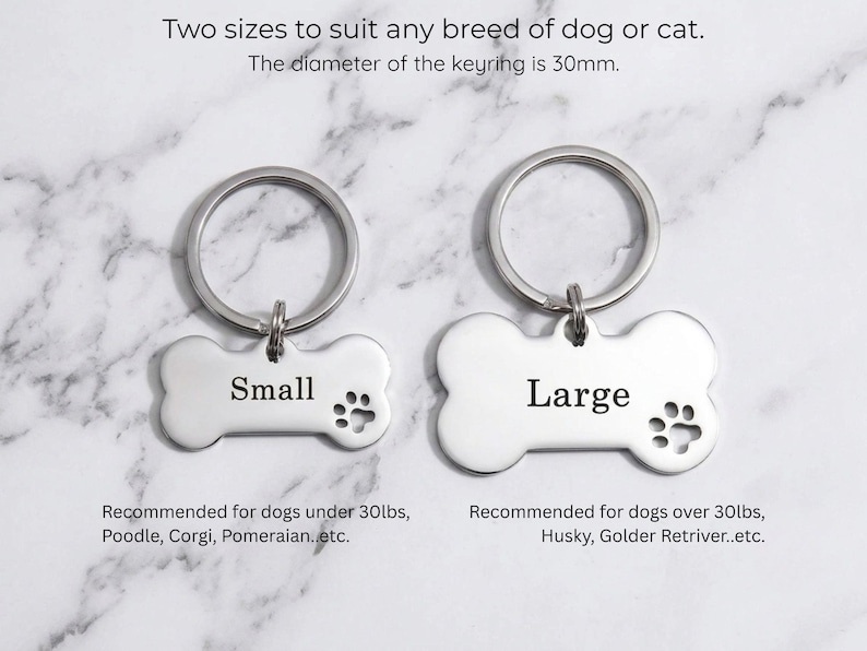 Custom silver pet ID tags for dogs showing small and large size options. Personalized bone-shaped engraved dog name tags with paw print detail on marble.
