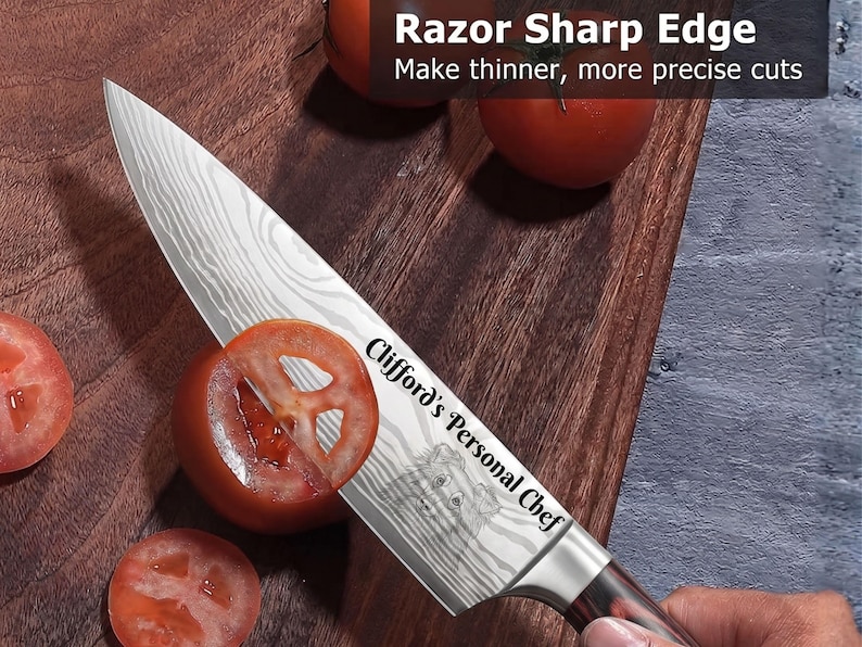 Personalized Damascus-style chef knife slicing a tomato on a wooden cutting board, custom laser engraved with the text "Clifford's Personal Chef" and a detailed dog portrait on the blade. Fresh tomatoes and a hand holding the knife demonstrate its razor-sharp edge in a kitchen setting.