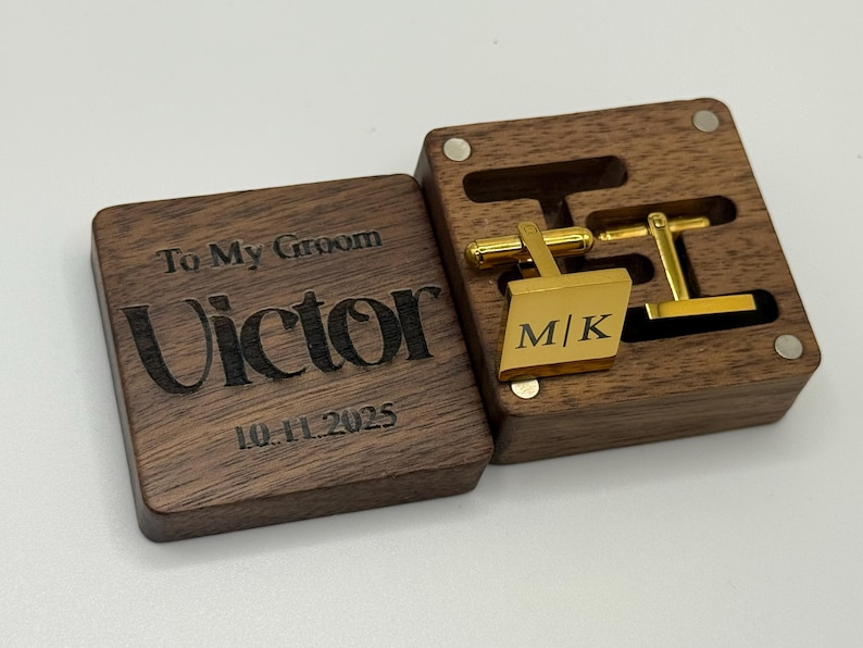 A wooden box with a hinged lid, engraved with "To My Groom" and the name "Victor" and the date "10.11.2025". Inside, gold cufflinks with the initials "M|K" are displayed in a fitted compartment. The box is open.