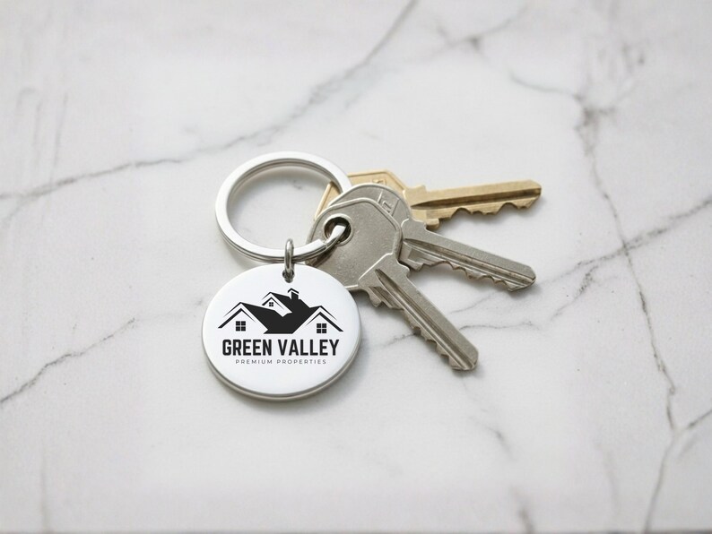 May include: A silver keychain with a round tag featuring the "Green Valley Premium Properties" logo in black. The keychain holds a set of keys. The background is a white marble surface.