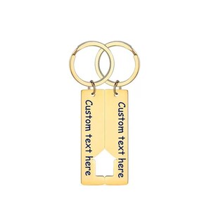 Two gold-colored keychains with a house-shaped design. Each keychain has a rectangular tag with the text "Custom text here" in blue. The keychains are connected by two gold-colored key rings.