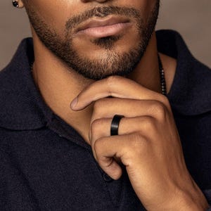 Close-up of a man wearing a matte black tungsten carbide wedding band on his ring finger, showcasing a modern minimalist comfort-fit ring.