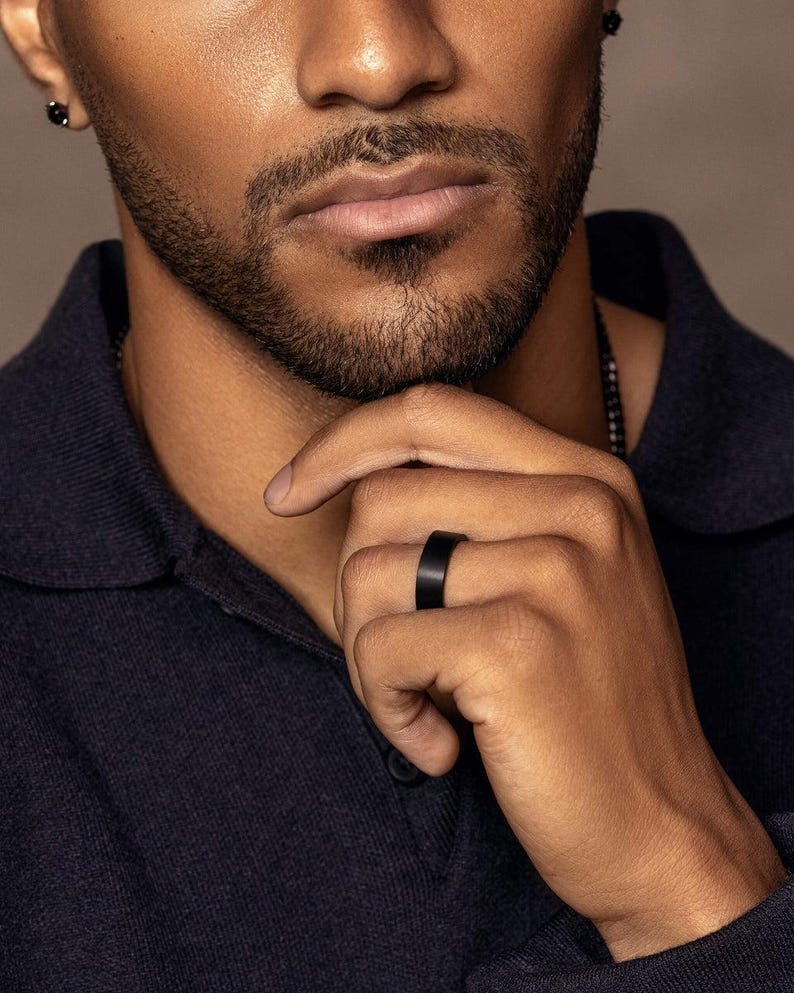 Close-up of a man wearing a matte black tungsten carbide wedding band on his ring finger, showcasing a modern minimalist comfort-fit ring.