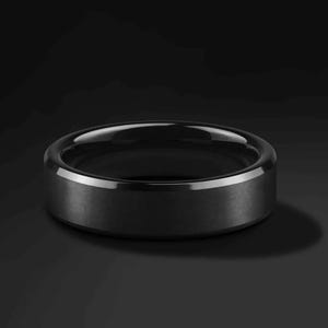 A black ring with a matte finish and a polished, beveled edge. The ring is set against a dark background, highlighting its sleek, modern design. This piece of jewelry is suitable for everyday wear.