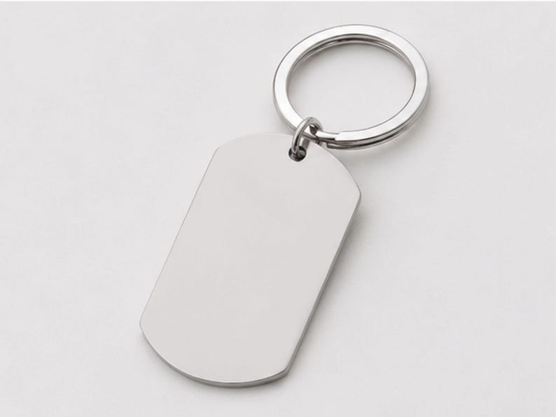 Close-up product photo of a blank silver stainless steel keychain with a polished finish. The dog-tag-style pendant is attached to a matching silver key ring and displayed on a clean light-gray background, emphasizing the customizable engraving surface for personalized handwriting, fingerprint, memorial messages, names, dates, logos, or custom text.